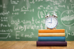 clock on stack of books with chalkboard in background